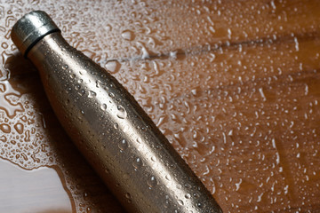 Stainless thermos bottle on a wooden table sprayed with water.