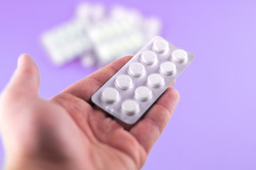 The man hand is holding a pack of white pills packed in blisters with copy space on purple background. Focus on foreground, soft bokeh