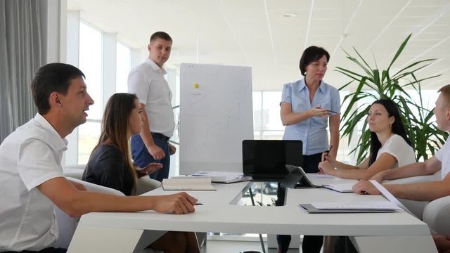 two people near flipchart offers ideas near business people listens presentation in conference room