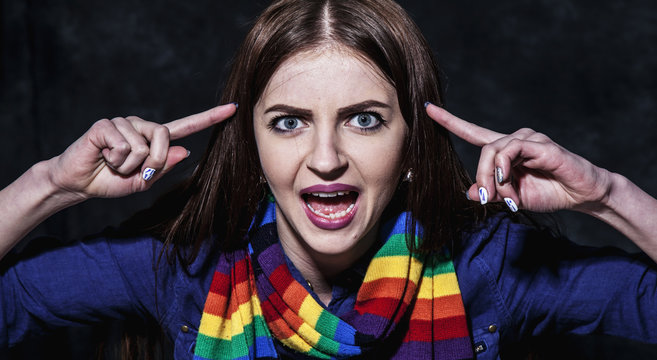 Beautiful serious Caucasian woman holding finger on his temple and having angry face as if saying: Are you crazy?  Use your brain, stop talking nonsense. Body language, psychology, gesture concept.