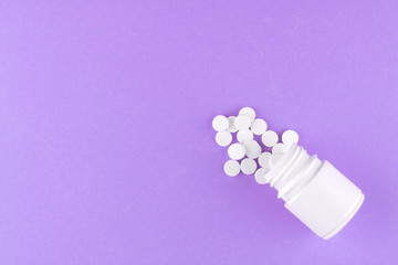 Close up white pill bottle with spilled out pills on purple background with copy space. Focus on foreground, soft bokeh. Pharmacy drugstore concept. Top view