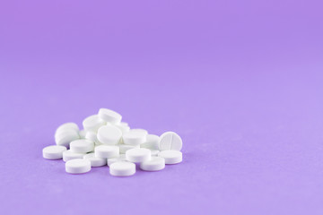 Obraz na płótnie Canvas Close up white pills on purple background with copy space. Focus on foreground, soft bokeh. Pharmacy drugstore concept