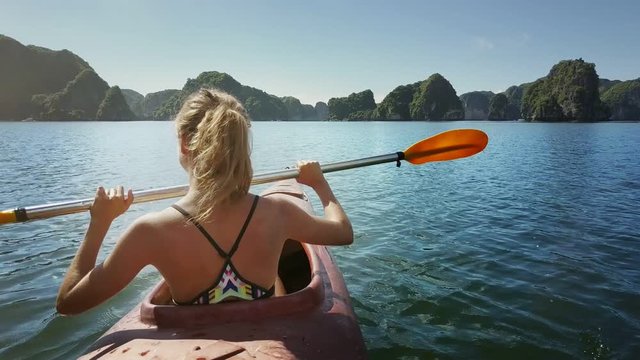 Backside Girl Rows Kayak with Paddle in Turquoise Ocean Bay