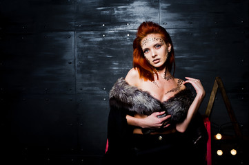 Fashion model red haired girl with originally make up like leopard predator against steel wall. Studio portrait on ladder.