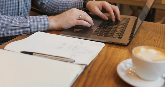 Close-up of a man's hand use laptop in the foreground of coffee and notebook in a cafe break businessman code business cup screen social media sitting