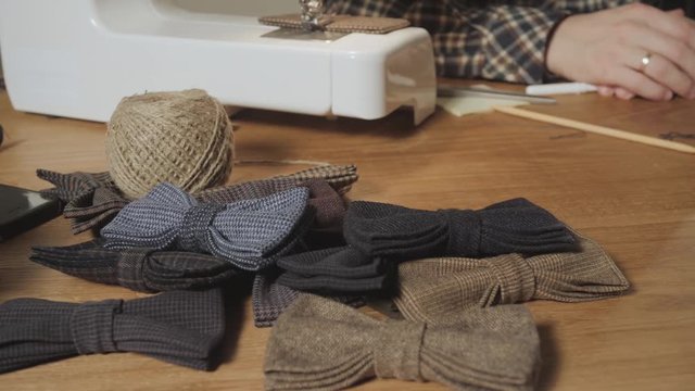 lots of ready made butterfly bow ties made of wool in the foreground, adds a finished product. Good looking young man working as a tailor and using a sewing machine in a textile studio.