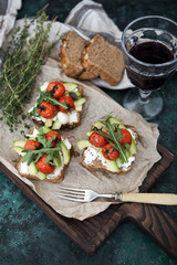 Set bruschette with grilled cherry tomatoes and avocado, with a glass of wine on a dark green background