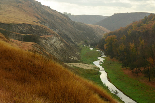 Beautiful landscape of the autumn forest in rainy day. Between the mountains a small river flows. Moldova, Edinet.