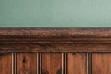 Old wooden skirting board against a green painted wall background texture.