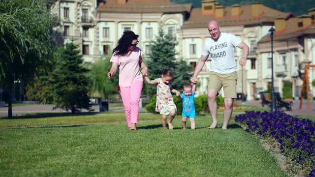 Carefree young Caucasian family happily runs along the green grass holding hands, happy faces of the family.