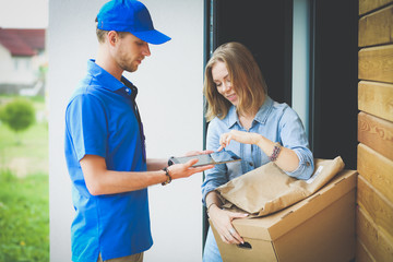Smiling delivery man in blue uniform delivering parcel box to recipient - courier service concept....