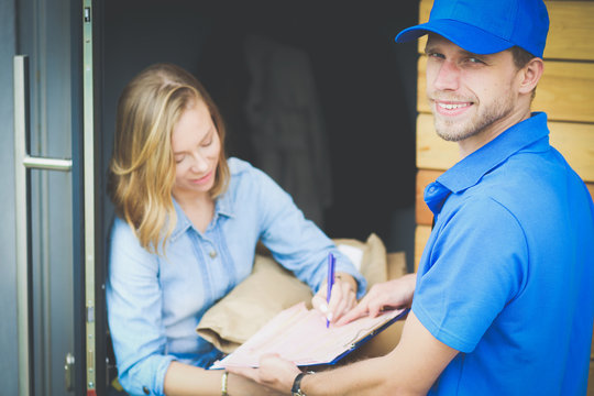 Smiling delivery man in blue uniform delivering parcel box to recipient - courier service concept. Smiling delivery man in blue uniform