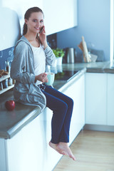 Woman using mobile phone sitting in modern kitchen.