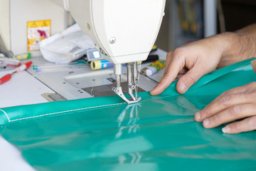 Men seamstress at the sewing machinesews the tarpaulin. Selective focus.