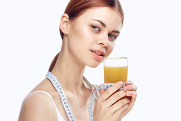 healthy lifestyle, freshly squeezed juice in the hand of a young woman with a measuring tape on a light background portrait