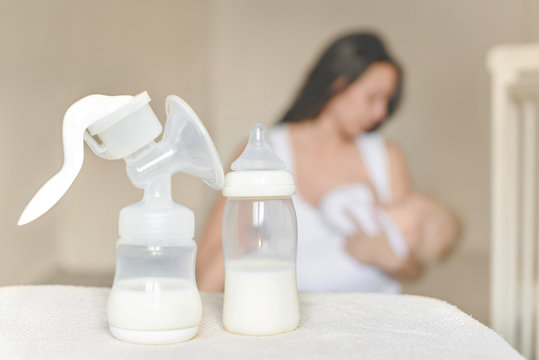 Manual breast pump and bottle with breast milk on the background of mother holding in her hands and breastfeeding baby. Maternity and baby care.
