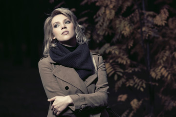 Young fashion woman in classic beige coat walking in autumn park