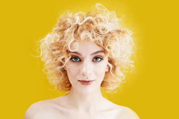 Portrait of a beautiful young girl with blonde curly hair close up on yellow background