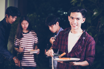 Asian group of friends having outdoor garden barbecue laughing with alcoholic beer drinks on night