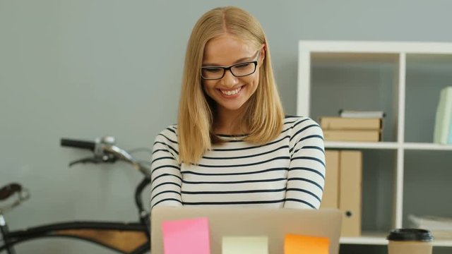 Portrait of attractive smiling business woman using laptop for working at the stylish office while sitting at the office table.