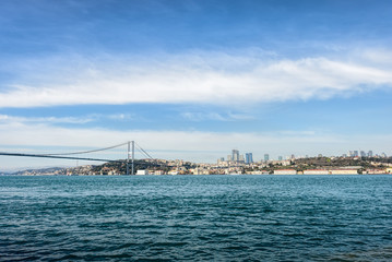 City coastline and bridge above sea under blue sky with white cl