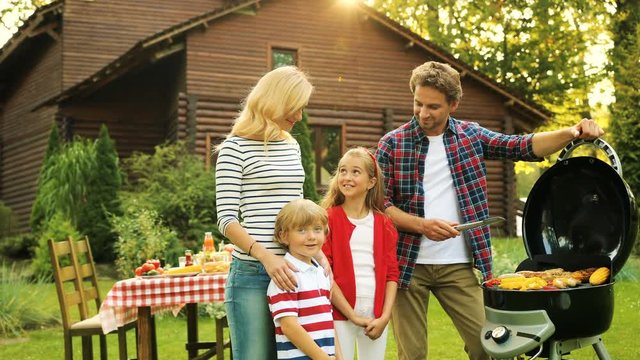Portrait of happy family near barbecue with vegetables. Modern wooden house in the beautiful green garden. Outdoor