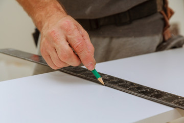Hand of a carpenter measures the distance using a builder's square and marks