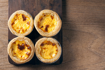 Delicious Egg tart, traditional Portuguese dessert, on wooden plate for coffee break on rustic wooden table.