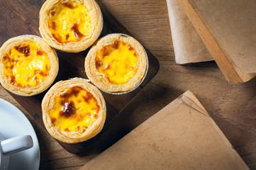 Delicious Egg tart, traditional Portuguese dessert, on wooden plate for coffee break on rustic wooden table.