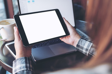 Mockup image of hands holding black tablet pc with white blank screen and laptop , coffee cup on wooden table background in cafe