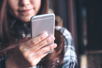 Closeup image of a beautiful Asian woman holding , using and looking at smart phone in modern cafe