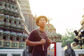 Young Asian traveling backpacker in Wat Pho with India inspired temple in Bangkok, Thailand