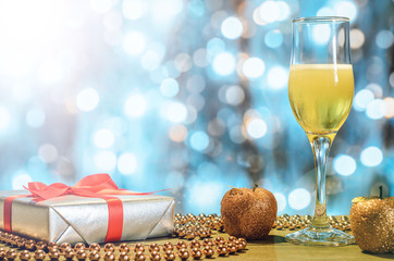 Christmas composition: a glass of champagne, gift, decor on a blurry, shiny background, free copy space