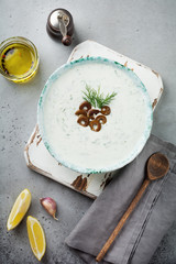 Traditional Greek sauce Tzatziki. Yoghurt, cucumber, dill, garlic and salt oil in a ceramic bowl on a gray stone or concrete background. Rustic style. Selective focus. Top view.