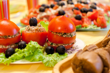 Covered table with fresh red stuffed tomatoes, lettuce and olives on white plate, bread and greek salad .