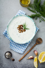 Traditional Greek sauce Tzatziki. Yoghurt, cucumber, dill, garlic and salt oil in a ceramic bowl on a gray stone or concrete background. Rustic style. Selective focus. Top view.