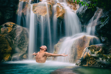 Fototapeta na wymiar Man relaxing with freedom open arms in waterfall in tropical nature. Wellness spa concept in holiday nature.