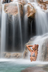 Waterfall woman relaxing in wellness nature water in tropical travel vacation background. Sexy bikini body care girl swimming in natural pool. Health and spa concept.