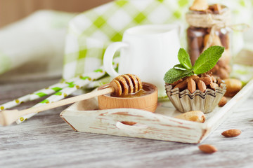 Honey in the wooden bowl, mint leaves, almonds and jar with milk on the wooden tray