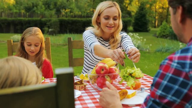 Family having a picnic at the green beautiful backyard in the summer. Outside. Wife putting a salad in his husband's plate
