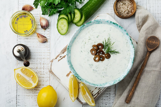Traditional Greek sauce Tzatziki. Yogurt, cucumber, dill, garlic and salt oil in a ceramic bowl on a light wooden background. Rustic style. Selective focus. Top view.