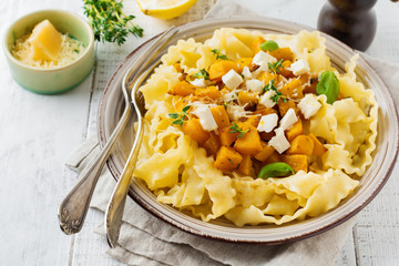 Pasta Mafaldine Napoletane with baked pumpkin, feta cheese and seasoning herbs in ceramic plate on white wooden background. Selective focus. Rustic style. Top view.