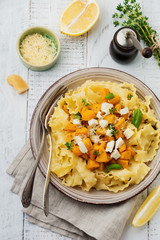 Pasta Mafaldine Napoletane with baked pumpkin, feta cheese and seasoning herbs in ceramic plate on white wooden background. Selective focus. Rustic style. Top view.