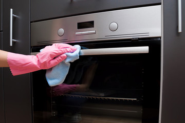 Employee hand in rubber protective glove with micro fiber cloth wiping an electric oven surface....