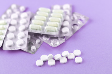 Full and empty packs of white capsules and pills packed in blisters with copy space on purple background. Focus on foreground, soft bokeh