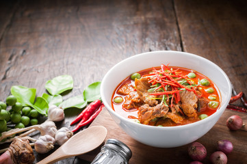 Red curry with pork and coconut milk, delicious Thai food on wooden table.