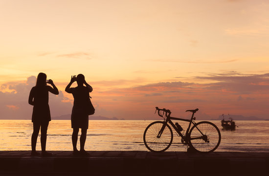 Silhouette bicycle and people take photo at beach sunset background