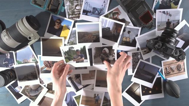 A woman looks at printed photos from travel spread on a wooden table with photo camera and lens.