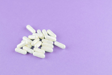 Close up white capsules on purple background with copy space. Focus on foreground, soft bokeh. Pharmacy drugstore concept