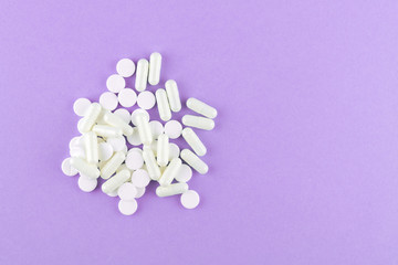 Obraz na płótnie Canvas Close up white pills and capsules on purple background with copy space. Focus on foreground, soft bokeh. Pharmacy drugstore concept. Top view